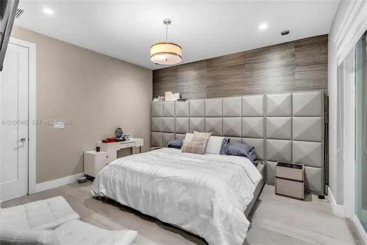 Custom wall-mounted upholstered grid headboard, horizontal wood-texture wall paneling, drum pendant light fixture, recessed ceiling lighting, and wood-finish flooring