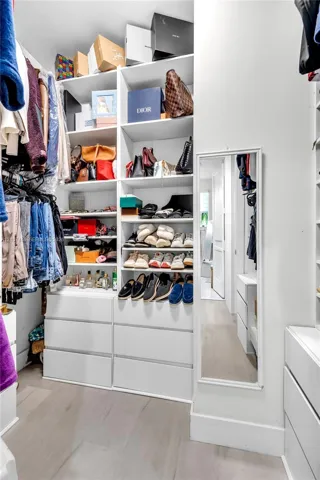 Walk-in closet featuring white custom built-in shelving, floor-to-ceiling storage units, multiple integrated drawer banks, and light-toned wood-finish flooring