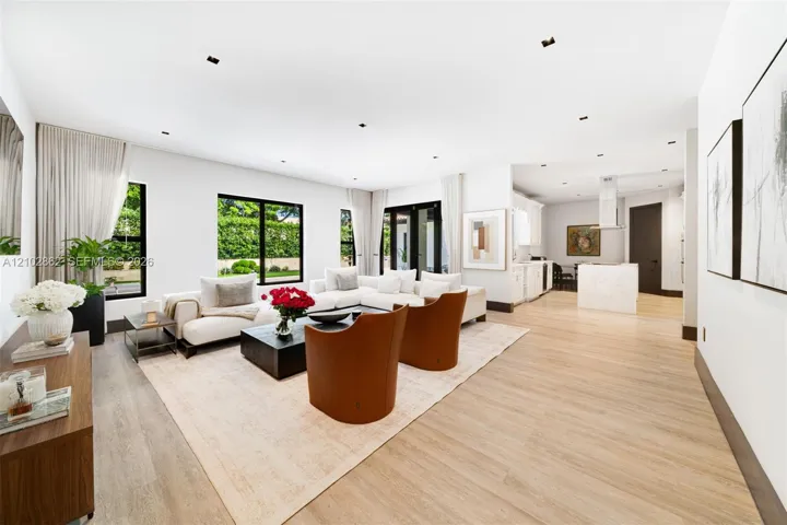 Open-concept interior featuring wood-finish flooring, recessed lighting, expansive windows with black frames, and a kitchen island with a stone-finish waterfall edge