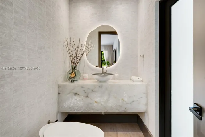 Floating stone vanity with a vessel sink, integrated LED-backlit organic-shaped mirror, and textured wall finish
