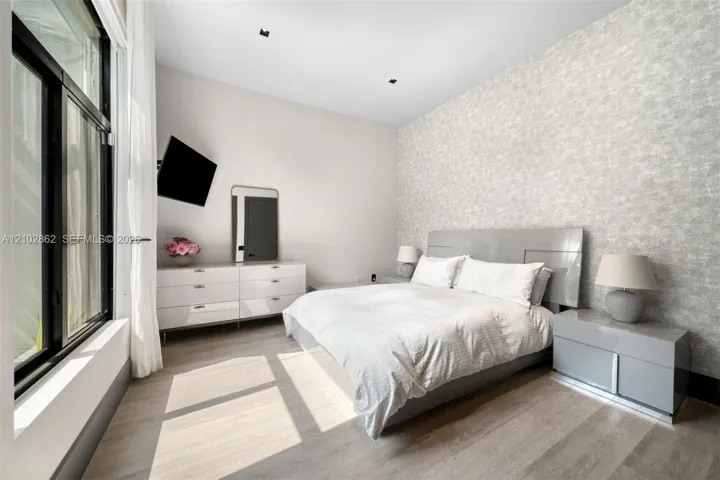 Bedroom featuring textured accent wall, floor-to-ceiling windows, recessed lighting, and wood-finish flooring