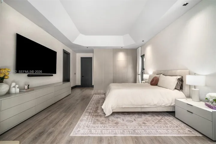 Tray ceiling with recessed lighting, integrated floor-to-ceiling cabinetry, wood-finish flooring, and minimalist flat-panel doors