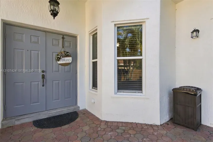 Entryway featuring a double-door entrance with paneled detailing, decorative exterior wall-mounted lighting, and a multi-toned paver porch