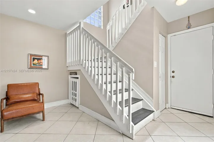 Foyer featuring ceramic tile flooring, a white staircase with dark treads and wood-finish railings, and glass block accent windows
