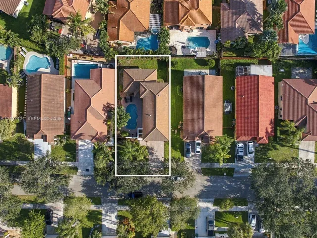 Aerial view of property featuring a tile roof, private swimming pool, paved driveway, and mature landscaping