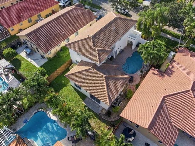 Aerial perspective of a two-story residence featuring a tile roof, an in-ground swimming pool, and stone paver decking