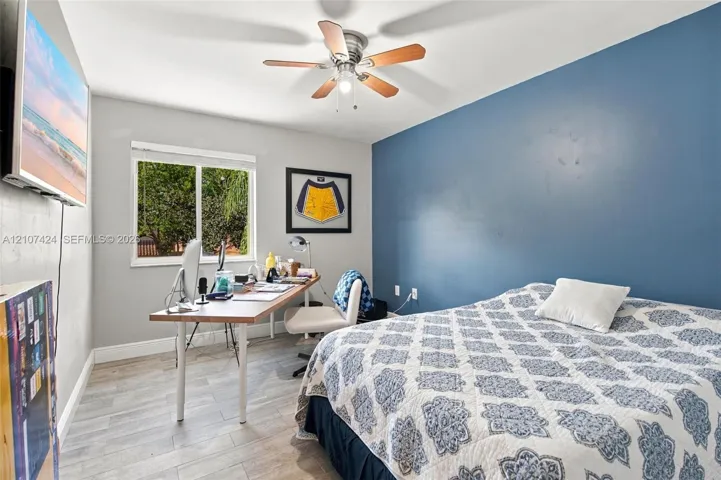 Bedroom featuring wood-finish flooring, a neutral color palette with a blue accent wall, a sliding window, and a ceiling fan with integrated lighting