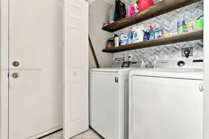 Laundry space featuring herringbone-patterned wall tile, dual wood-finish floating shelves, and a bi-fold closet door on 1st floor