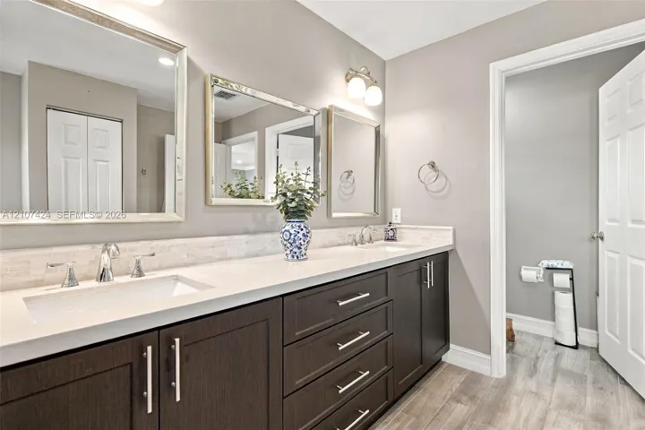 Double vanity featuring dark espresso cabinetry, stone-finish countertops, dual rectangular undermount sinks, polished chrome hardware, and three separate rectangular mirrors