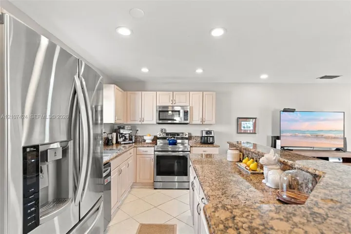Kitchen featuring stone-finish countertops, stainless steel refrigerator, built-in microwave, range, and recessed lighting