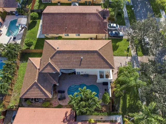 Aerial perspective of a multi-gabled residence featuring a concrete tile roof, paver patio, in-ground swimming pool, and landscaped perimeter