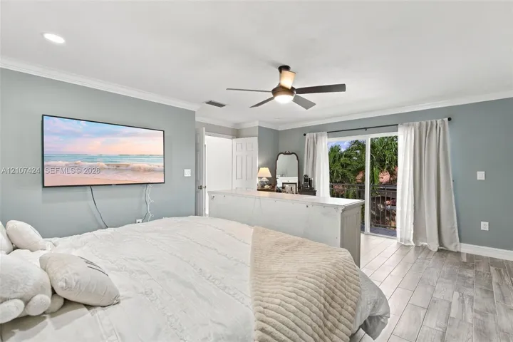 Living space featuring wood-finish tile flooring, crown molding, a central ceiling fan with integrated lighting, and a sliding glass door providing external access