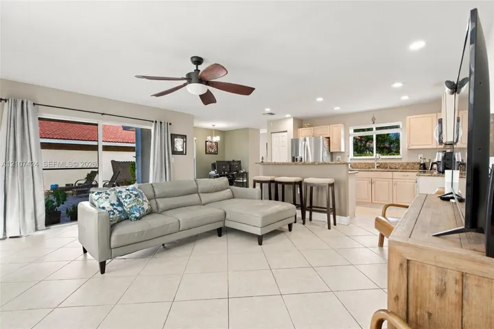 Open-concept interior featuring light-toned tile flooring, recessed ceiling lighting, a multi-blade ceiling fan, and sliding glass doors