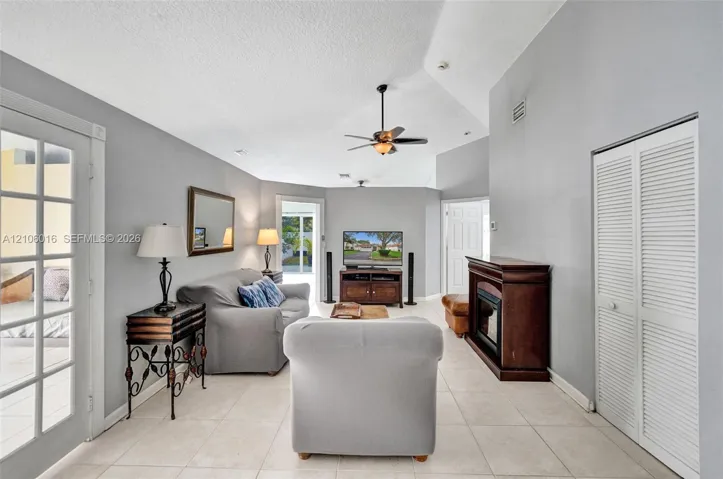 Living area featuring vaulted ceilings, large-format tile flooring, a fireplace with a wood-finish mantel, louvered closet doors, and glass-paned double doors