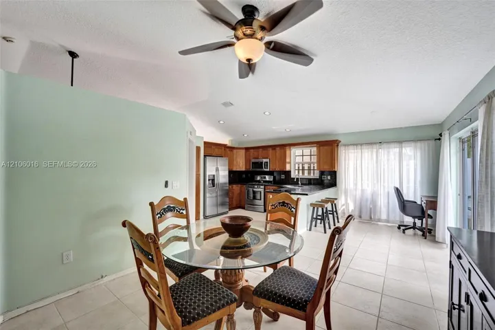 Vaulted ceiling featuring a central ceiling fan with integrated lighting, wood cabinetry, stainless steel appliances, ceramic tile flooring, and recessed lighting