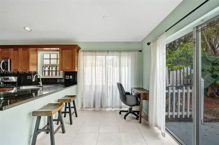 Kitchen featuring wood cabinetry, stone countertops, recessed lighting, tile flooring, and sliding glass doors
