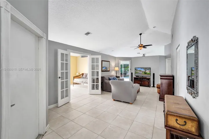 Living area featuring vaulted ceilings, light-toned tile flooring, French doors with glass panes, and a ceiling fan with light fixture