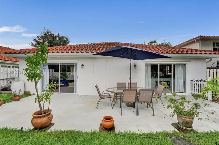 Concrete patio area featuring dual sliding glass doors, exterior wall-mounted lighting, and a terracotta tile roof