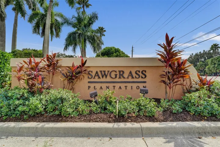 Community entrance monument featuring stucco masonry construction, dimensional lettering, landscape lighting, and mature tropical foliage