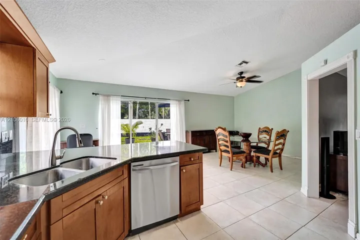 Kitchen featuring wood cabinetry, stone-finish countertops, an undermount stainless steel sink, and a stainless steel dishwasher, with ceramic tile flooring throughout