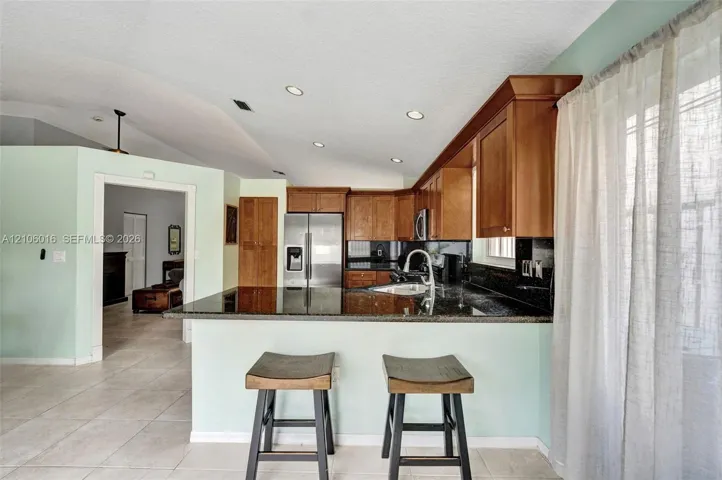 Kitchen featuring wood cabinetry, stone-surface countertops, tile flooring, stainless steel refrigerator, and recessed lighting