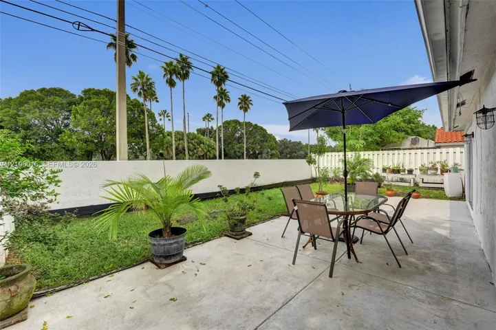 Concrete patio area featuring a low-maintenance lawn, white perimeter wall, and exterior wall-mounted light fixtures