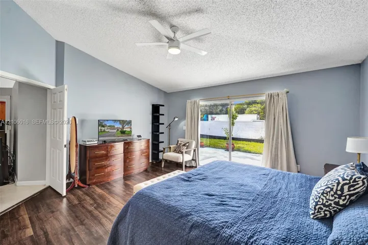 Vaulted ceiling with a central multi-blade ceiling fan, wood-finish flooring, and sliding glass doors providing outdoor access