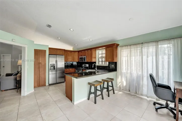 Kitchen featuring wood cabinetry, stainless steel appliances, dark stone-finish countertops, ceramic tile flooring, and recessed lighting