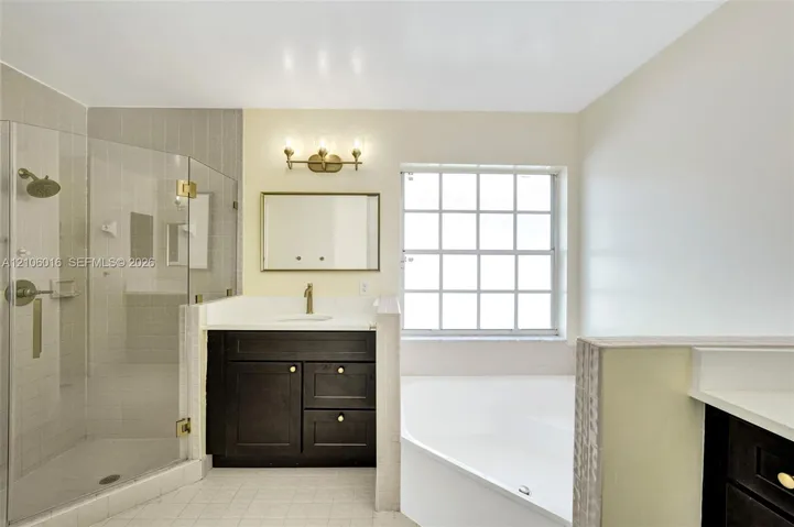 Bathroom featuring a glass-enclosed shower, a dark-finish vanity with a light-tone countertop, a soaking tub, and a multi-pane window
