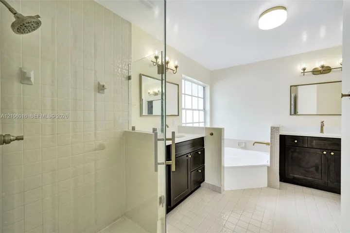 Bathroom featuring a walk-in shower with glass enclosure, dual dark-finish vanities with light-toned solid surface countertops, and a built-in soaking tub