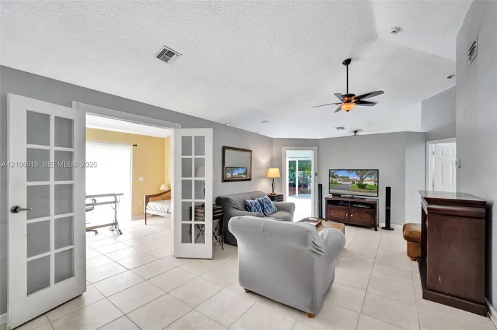 Living area featuring vaulted ceilings, light-tone tile flooring, French doors, and dual ceiling fans