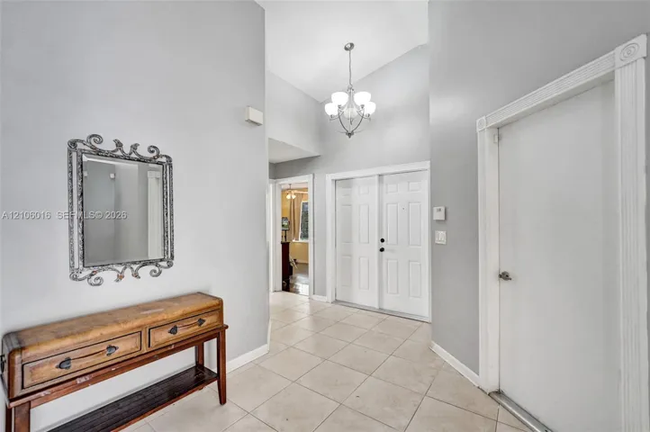 Foyer featuring vaulted ceilings, neutral ceramic tile flooring, double-door entry, and a multi-light chandelier