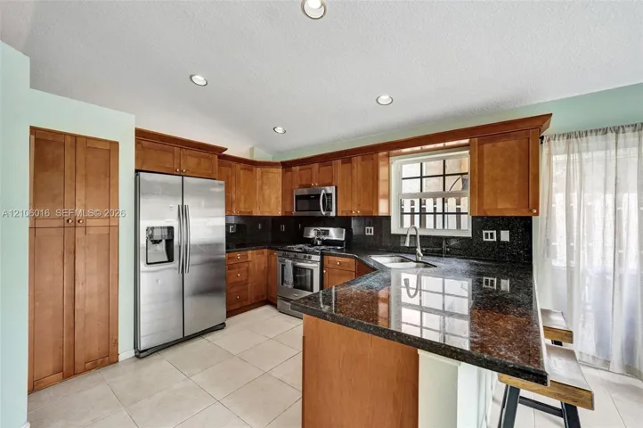 Kitchen featuring wood cabinetry, stone countertops, stainless steel appliances, tiled flooring, and recessed lighting