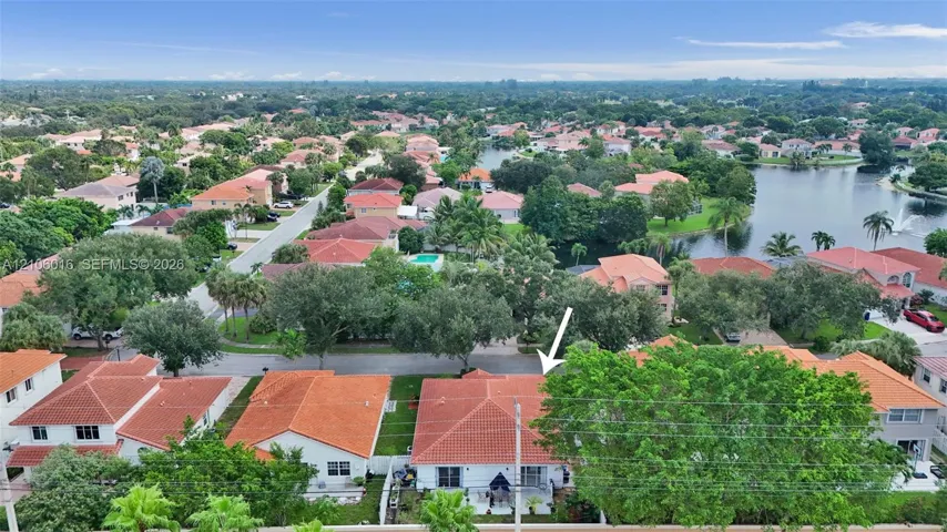 Aerial perspective of a single-story residence featuring a terracotta tile roof and mature tree canopy situated within a neighborhood setting
