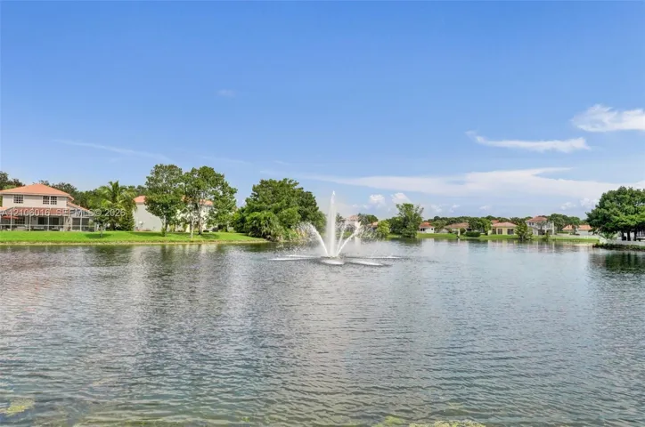 Waterfront pond featuring a central fountain, manicured lawn, and mature landscaping