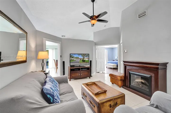 Vaulted ceilings, tiled flooring, and a fireplace with a dark wood-finish mantel