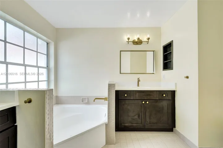 Bathroom featuring a soaking tub, a single-sink vanity with a solid-surface countertop, dark cabinetry, and a wall-mounted light fixture