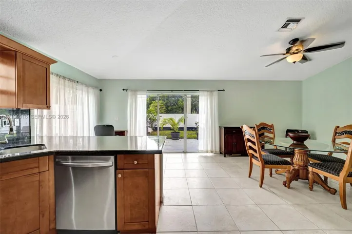 Kitchen featuring light wood-finish cabinetry, solid-surface countertops, stainless steel dishwasher, tile flooring, and a ceiling fan