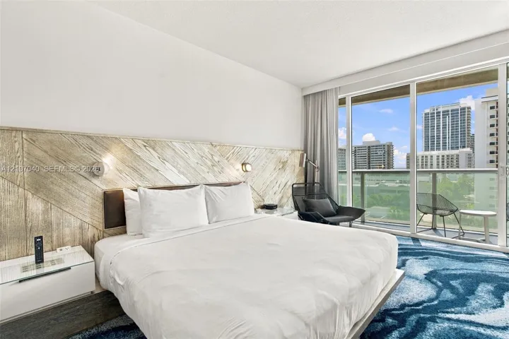Floor-to-ceiling glass sliding doors opening to a private balcony, custom wood-paneled accent wall, and wall-mounted reading lights