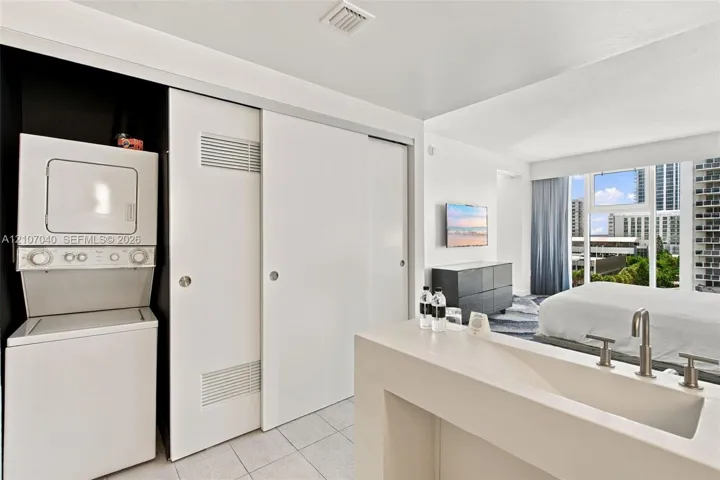 Stacked washer and dryer unit, built-in floor-to-ceiling sliding closet doors, and custom white vanity with integrated basin and polished metal faucet