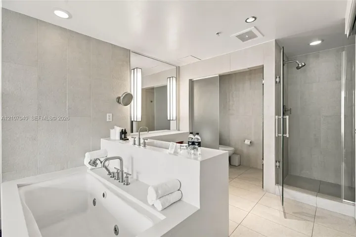 Jetted soaking tub with polished chrome fixtures, walk-in glass-enclosed shower, large-format tile wall cladding, and recessed lighting