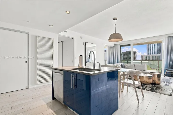 Kitchen island featuring high-gloss blue cabinetry, a stainless steel undermount sink, a gooseneck faucet, and light-toned tile flooring