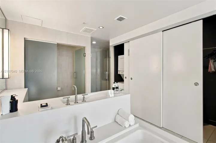Modern bathroom featuring a rectangular vessel sink with a bridge-style faucet, white solid-surface countertop, walk-in glass shower enclosure, and sliding panel doors