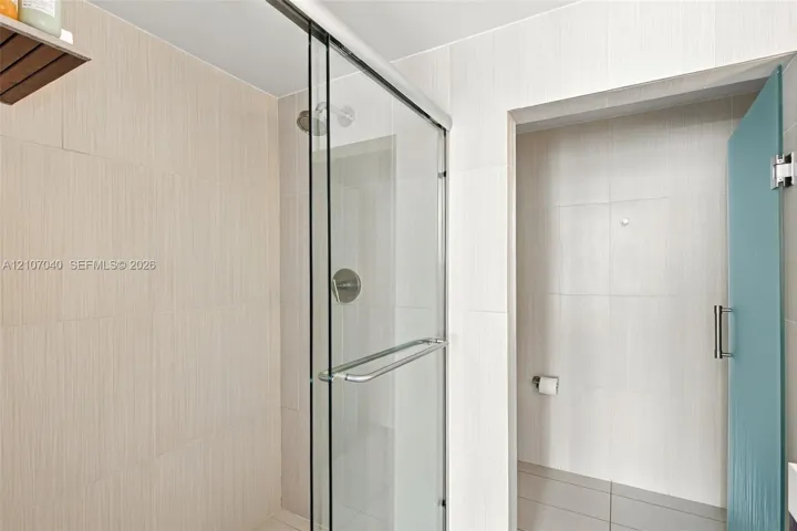 Walk-in shower featuring floor-to-ceiling neutral tile, a frameless glass sliding door, polished chrome fixtures, and a glass-paneled entry door
