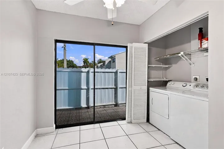 Utility room featuring ceramic tile flooring, a ceiling fan, sliding glass door, and louvered closet doors with integrated wire shelving