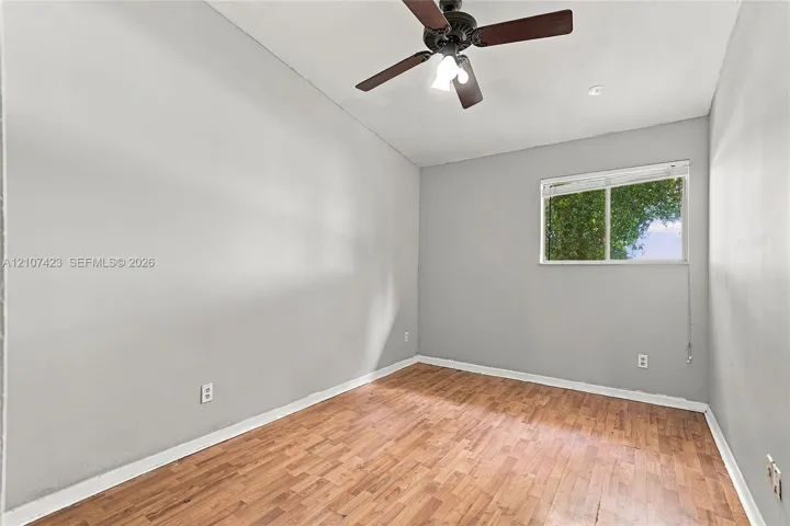 Room with wood-finish flooring, neutral wall paint, vaulted ceiling, multi-blade ceiling fan with integrated lighting, and horizontal sliding window