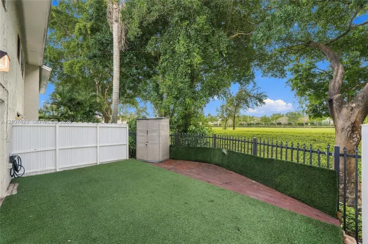 Backyard featuring synthetic turf, decorative brick-finish hardscaping, white vinyl perimeter fencing, and black metal perimeter railings