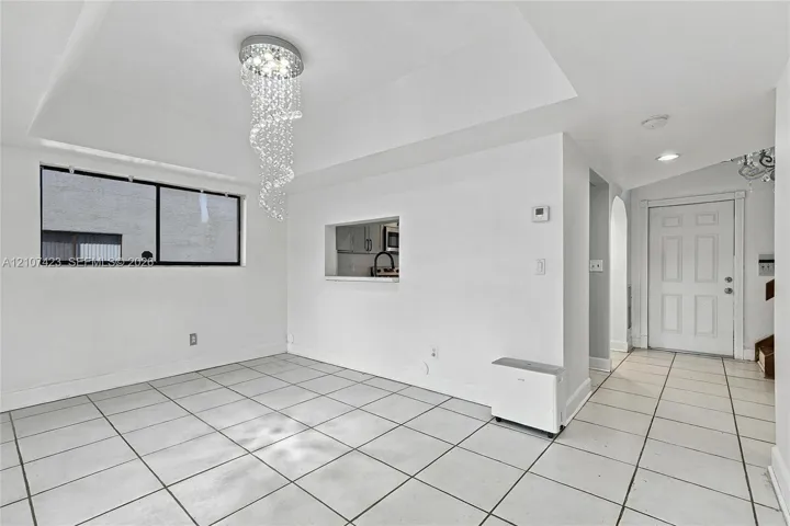 Open interior space featuring large-format ceramic tile flooring, a recessed ceiling with a crystal drop chandelier, and a cut-out wall opening