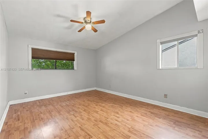 Vaulted ceiling featuring a central wood-finish ceiling fan with integrated lighting, wood-finish flooring, and dual windows