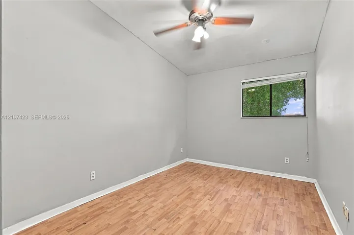 Interior room featuring wood-finish flooring, neutral wall tones, a ceiling fan with integrated lighting, and a single-pane window